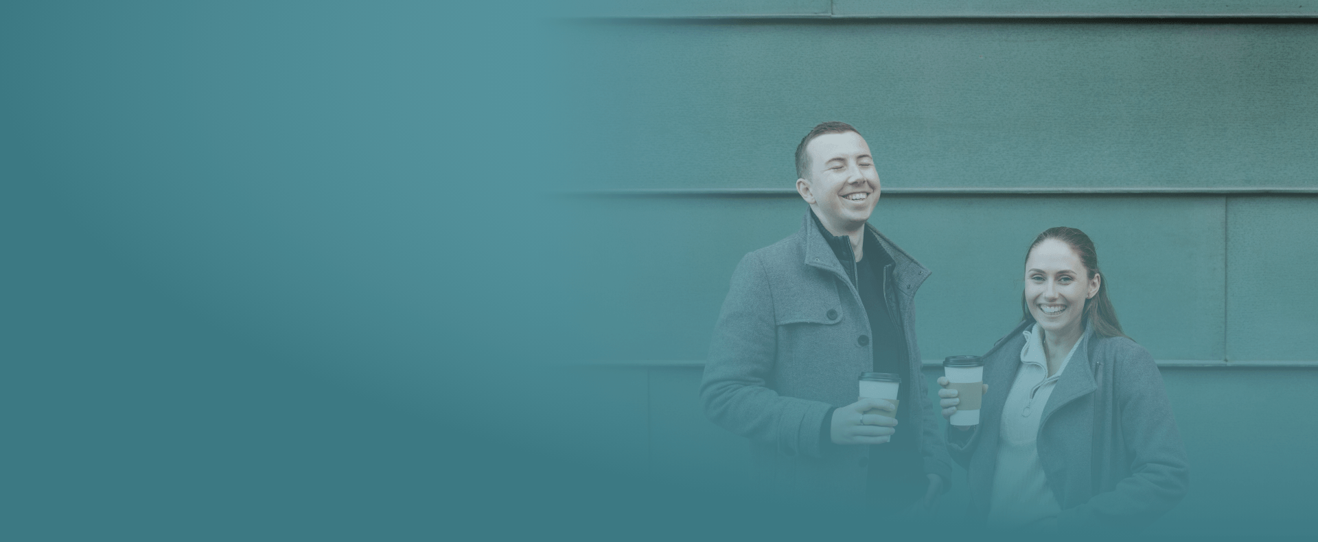 Yase und Lukas lachen mit einem Kaffee in der Hand.