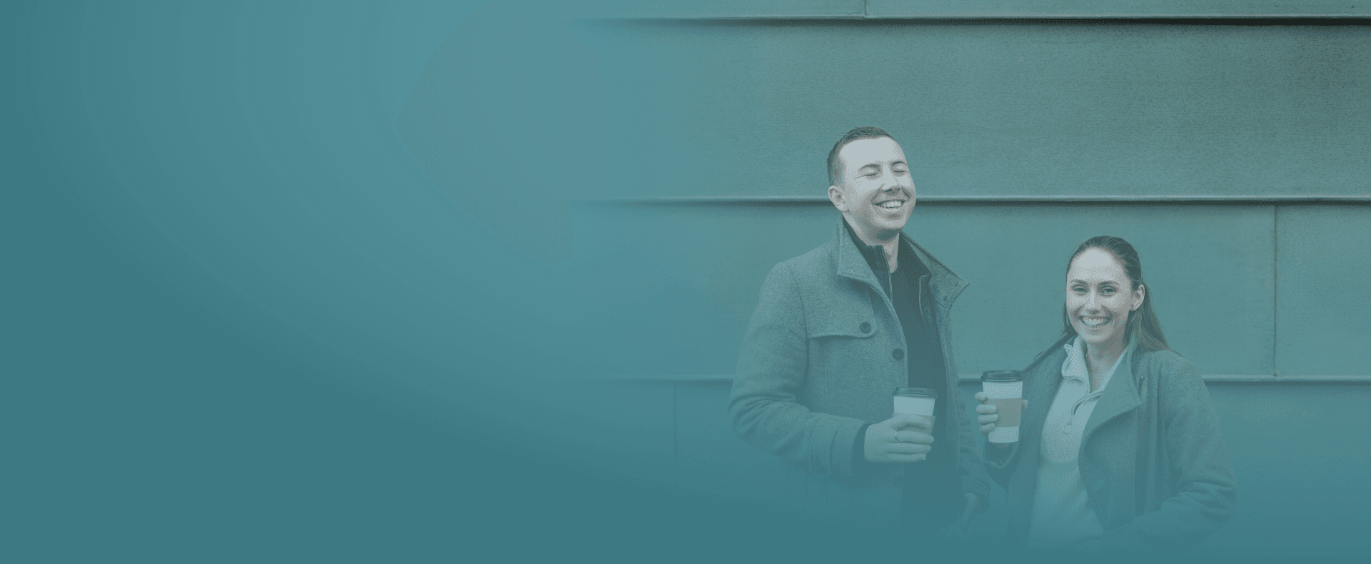 Yase und Lukas lachen mit einem Kaffee in der Hand.